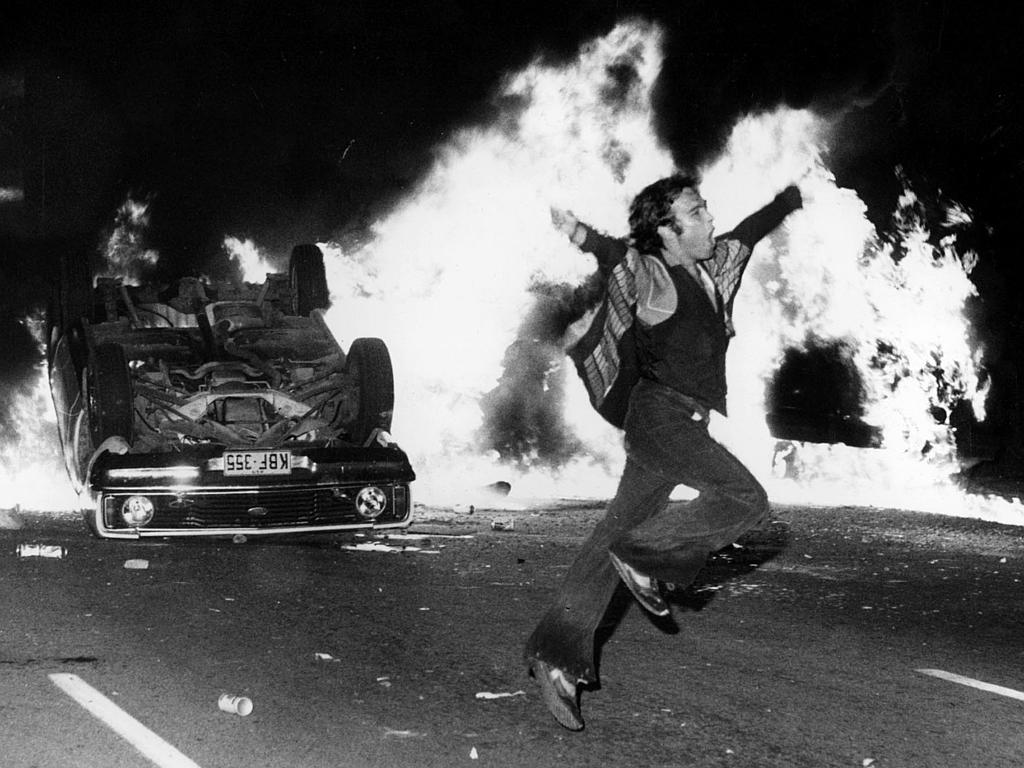 This meme is an image of a person in the midst of a chaotic and violent scene, likely a riot or protest. The image shows a person in a panicked state, with a shocked expression and their arms raised in a defensive or fleeing position. The text "BREAKING: Person in the middle of a riot is still alive" is likely a humorous commentary on the absurdity of the situation.